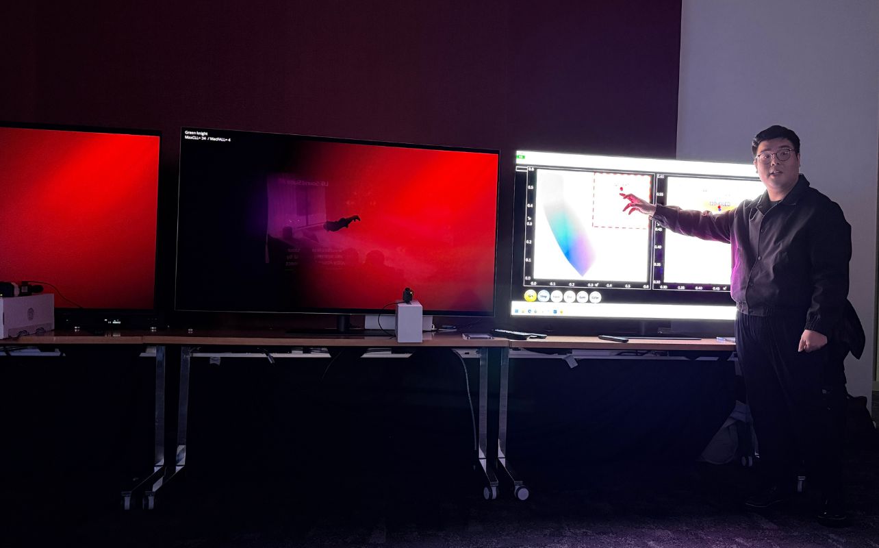 An LG rep is showing off different colour levels in a dark setting on 3 TV panels.