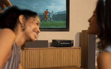 Two women smiling in front of a Denon AVRX2900 AV receiver.