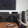 A man sitting in the corner of a living room turning on a TV with a Denon AX1700 AV receiver under the display.