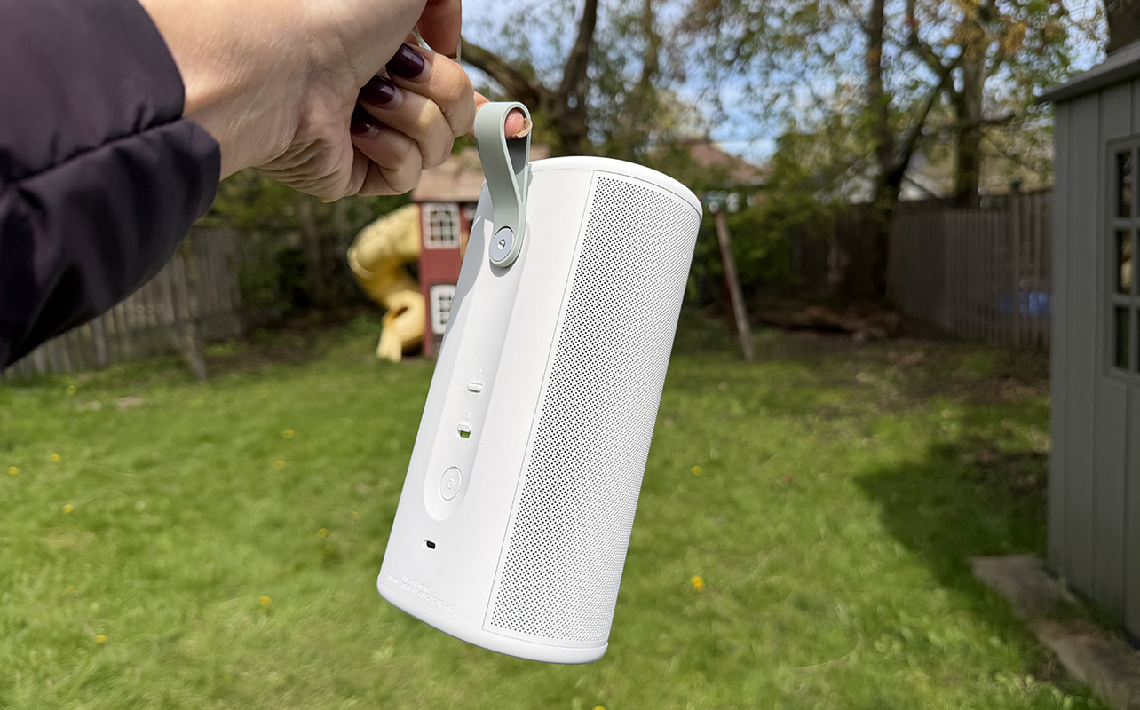 A hand holding the utility strap of the Sonos Play speaker outside, showing the back.
