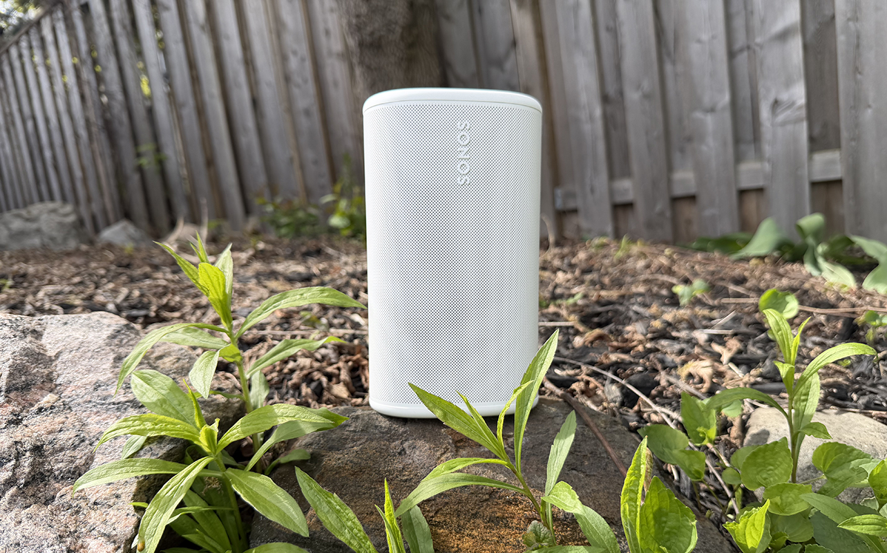A Sonos Play speaker outside on a rock in a garden.