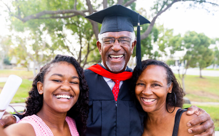 A senior man graduates with his master's degree and takes a photo with his family