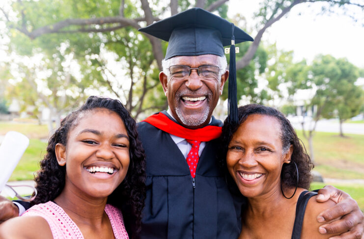 A senior man graduates with his master's degree and takes a photo with his family