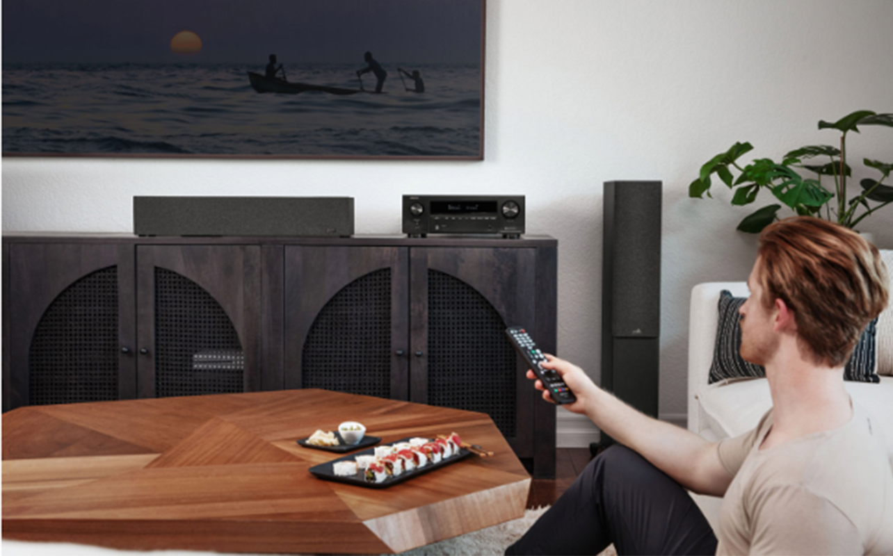 A person adjusting the Denon AVR-X1700H receiver on the remote control.