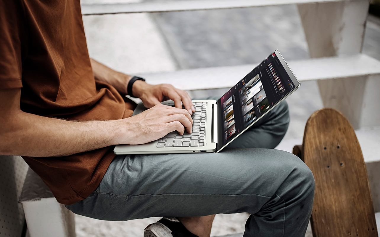 Student with skateboard nearby using laptop with Zoom call outside.