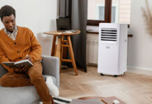 A man sitting on the couch with a Black & Decker portable air conditioner by the window.