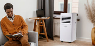 A man sitting on the couch with a Black & Decker portable air conditioner by the window.