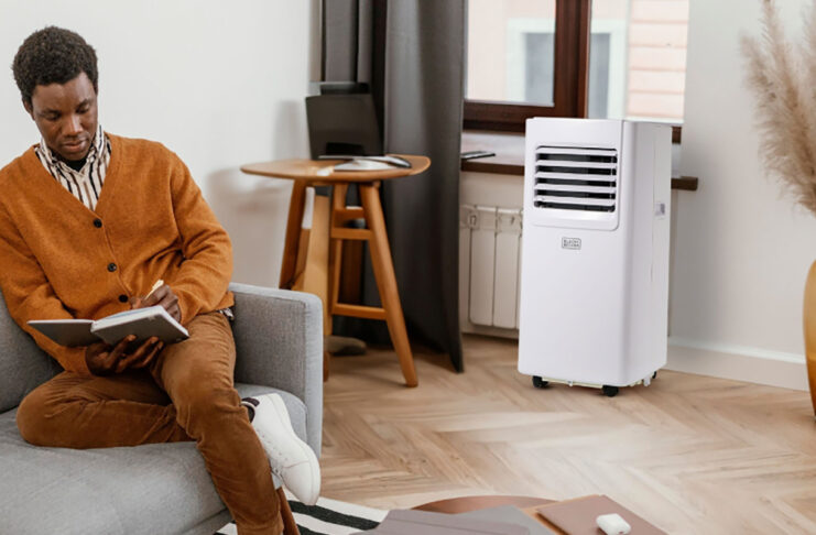 A man sitting on the couch with a Black & Decker portable air conditioner by the window.