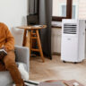 A man sitting on the couch with a Black & Decker portable air conditioner by the window.