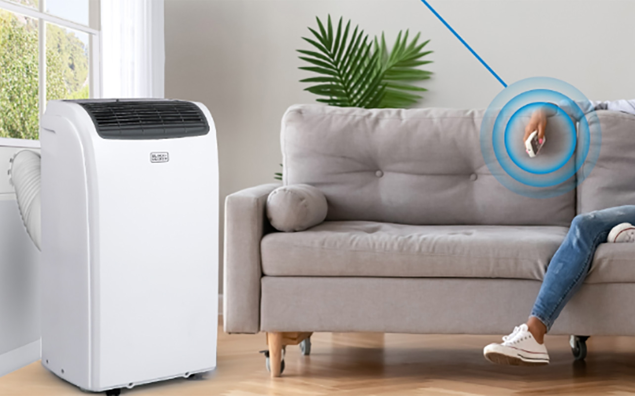 A woman relaxing on the couch with a Black & Decker portable air conditioner in the corner.