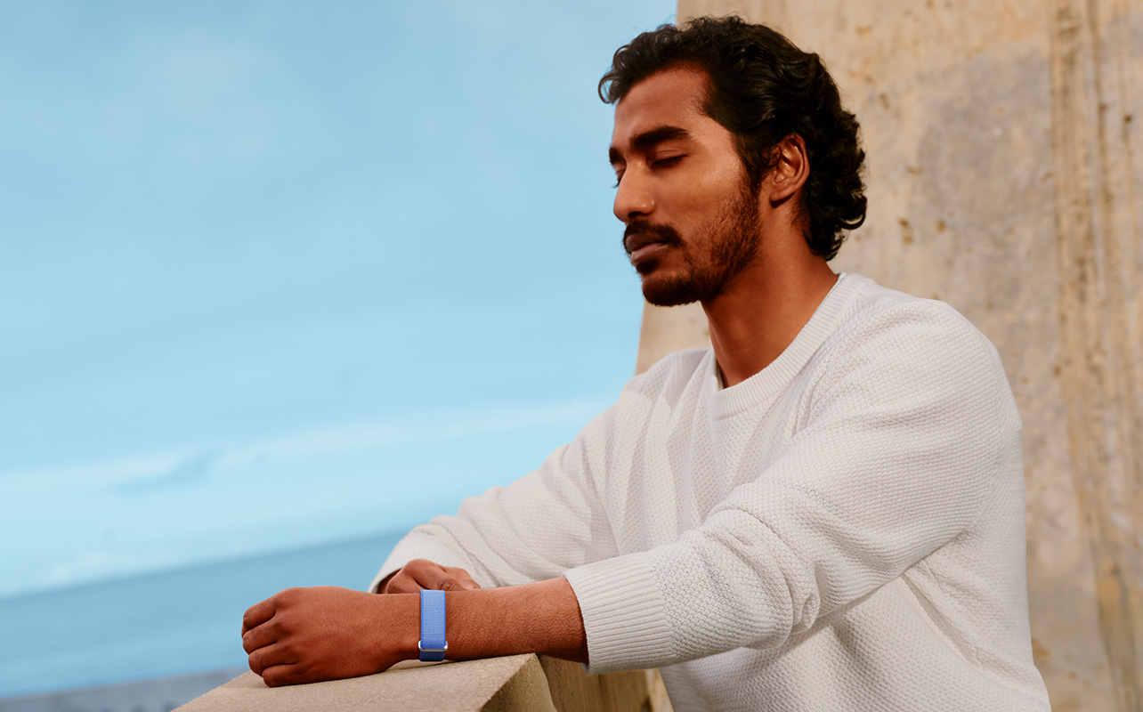 A man standing on a balcony with his eyes closed wearing the Fitbit Air.