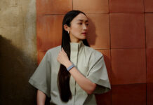 A woman with long hair standing against a wall wearing the Fitbit Air.
