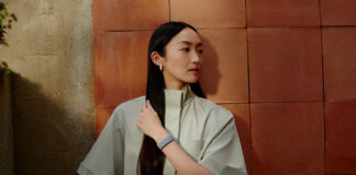 A woman with long hair standing against a wall wearing the Fitbit Air.