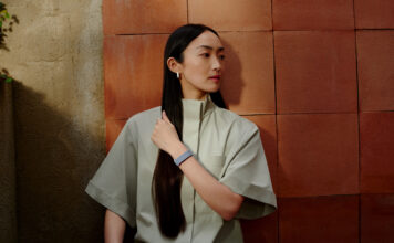 A woman with long hair standing against a wall wearing the Fitbit Air.