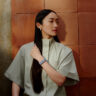 A woman with long hair standing against a wall wearing the Fitbit Air.