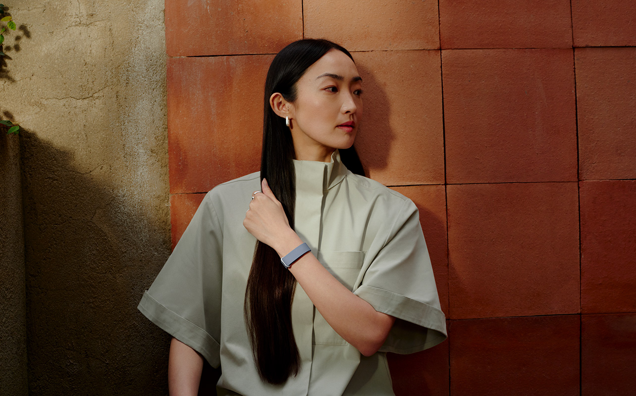 A woman with long hair standing against a wall wearing the Fitbit Air.