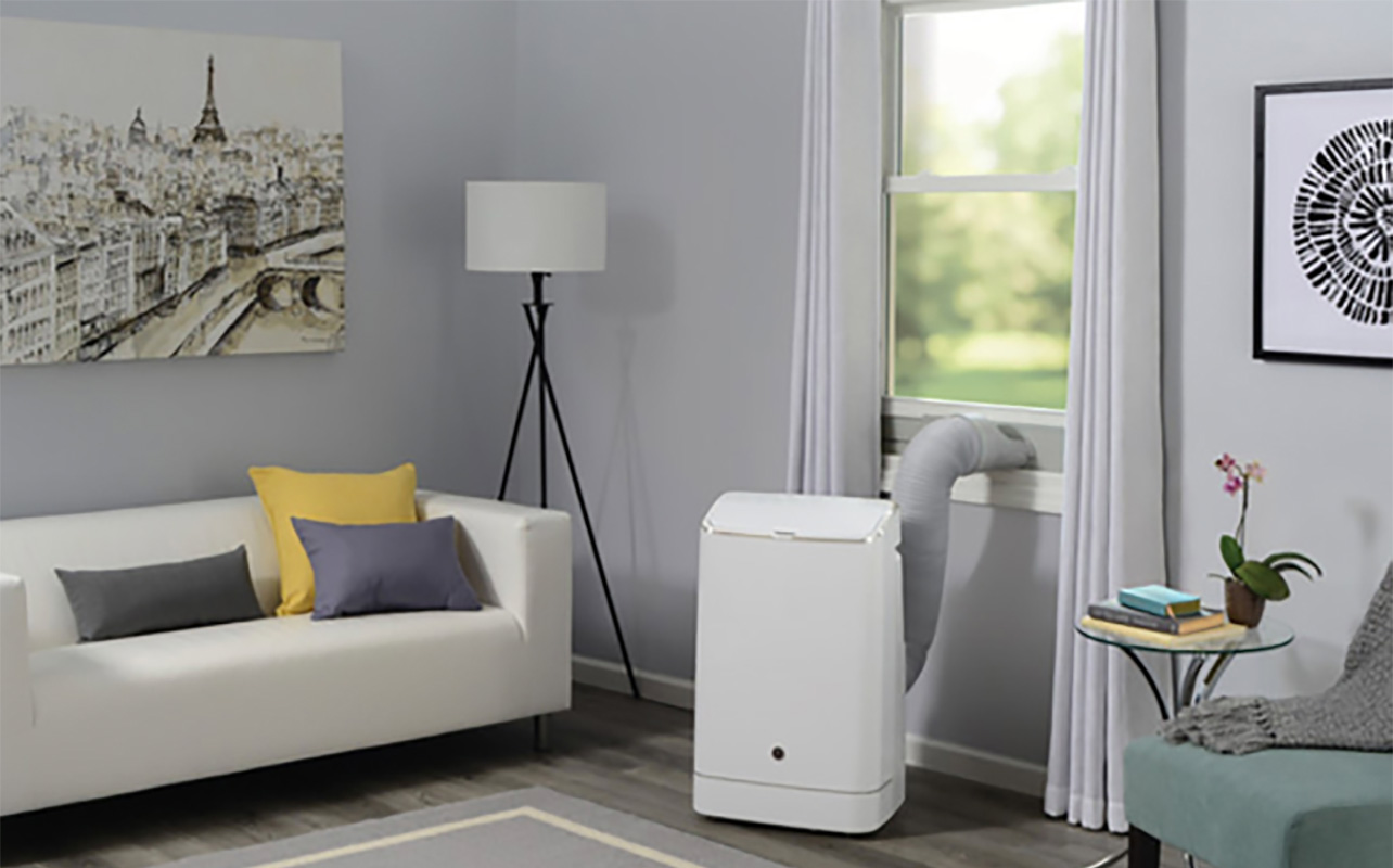A GE portable air conditioner set up in a living room by a window.