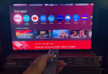 A hand holding the remote in front of the Hisense 65UR9SG RGB mini LED TV.