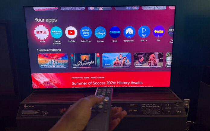 A hand holding the remote in front of the Hisense 65UR9SG RGB mini LED TV.