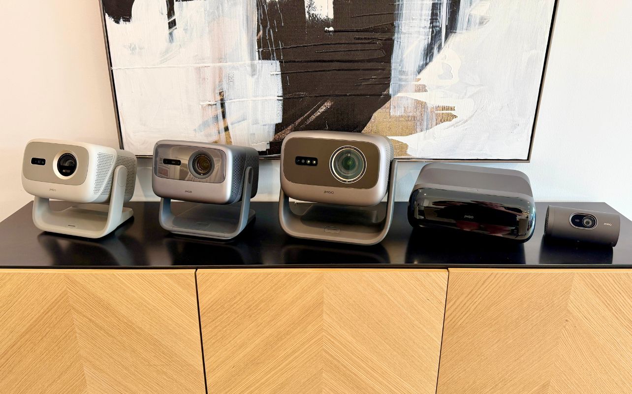 The full line of five JMGO projectors is displayed on a black tabletop with a painting in the background.