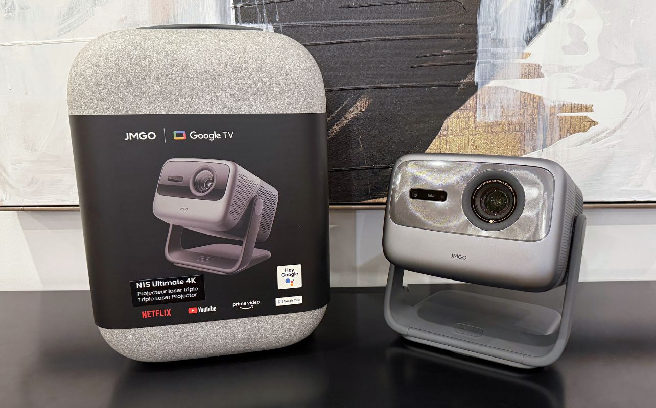 A retail box and the NIS Ultimate 4K projector are sitting next to each other on a black tabletop with a painting in the background.