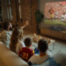 A family watching TV in the living room with the Epson Lifestudio Grand Plus projector.