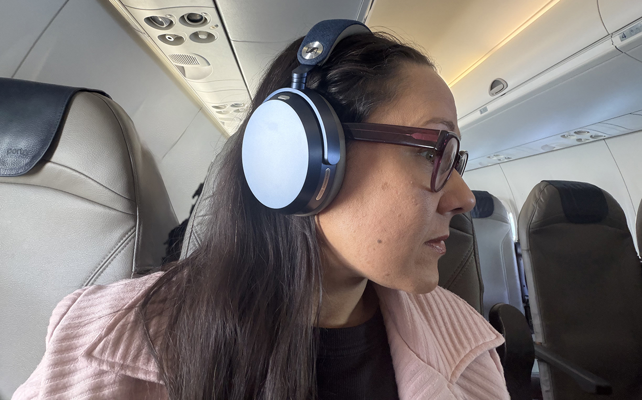 A woman sitting on a plane wearing the Sennheiser Momentum 5 Wireless headphones.