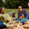 A group of young people having a picnic with he Xgimi Vibe One portable projector in the middle.