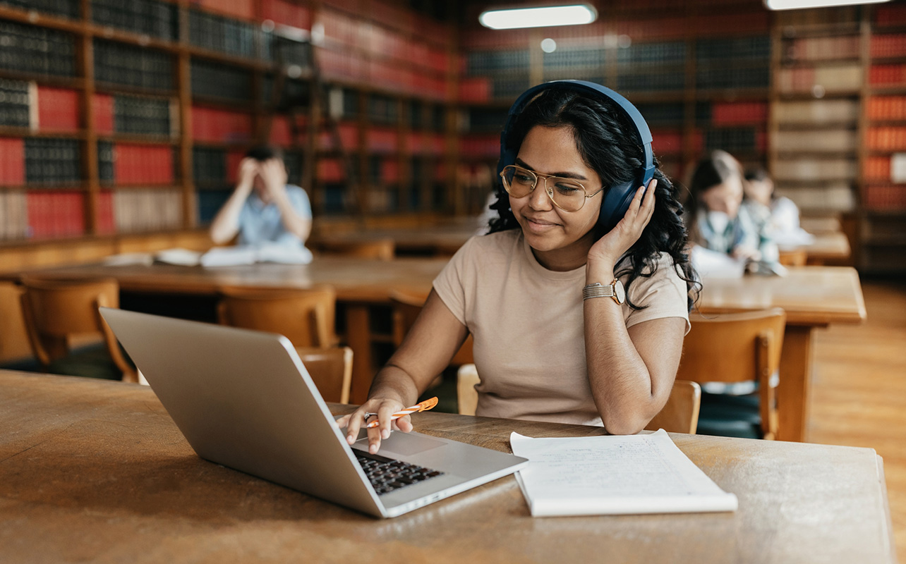 Student wearing headphones studying with laptop in library