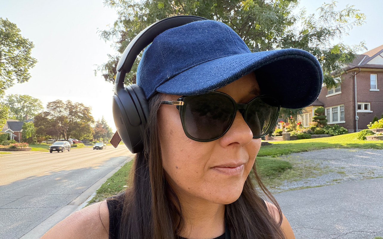 A woman wearing a blue hat and the Bose QuietComfort 2 headphones walking on a busy street.