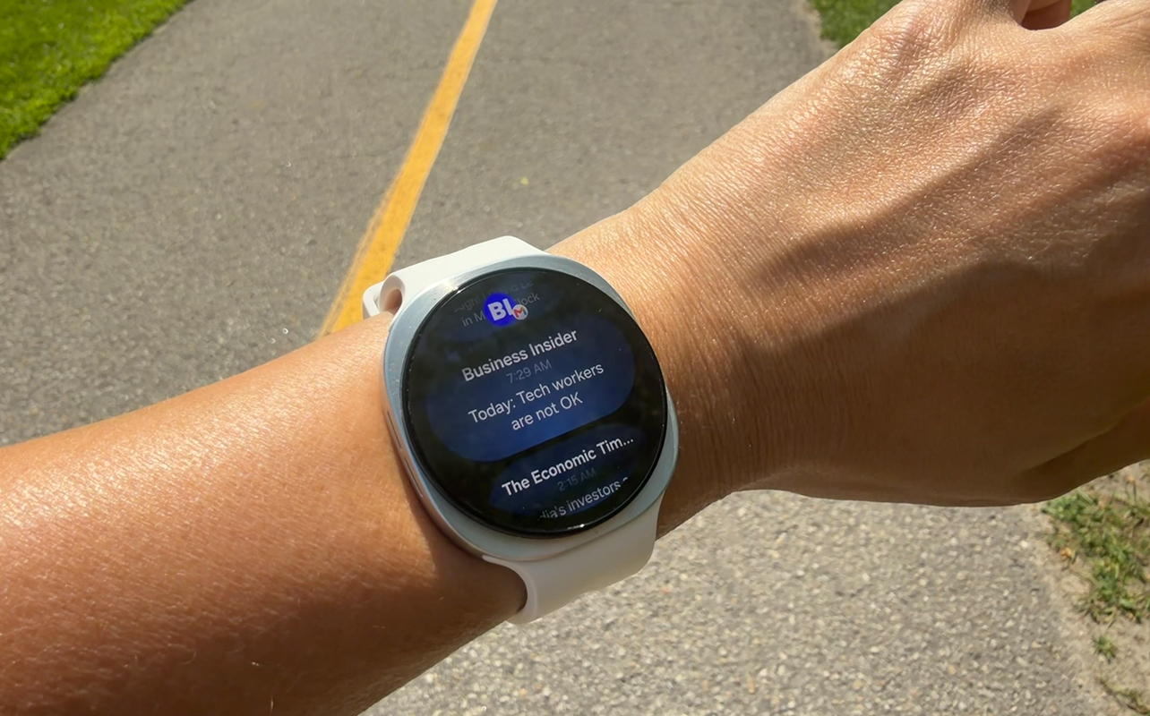 A Samsung Galaxy Watch 9 on a wrist outside showing a news update. 