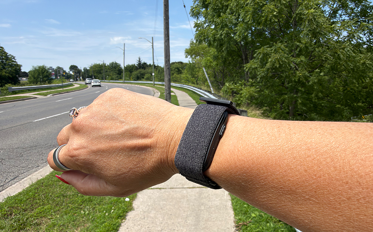 A hand held out on a sidewalk by the road, wearing the Garmin CIRQA smart band.
