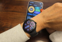 The Google Pixel Watch 5 on an arm with the Google Pixel 11 Pro in the background showing the Google Health app