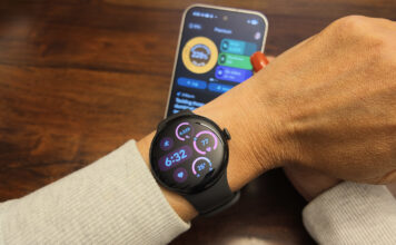 The Google Pixel Watch 5 on an arm with the Google Pixel 11 Pro in the background showing the Google Health app