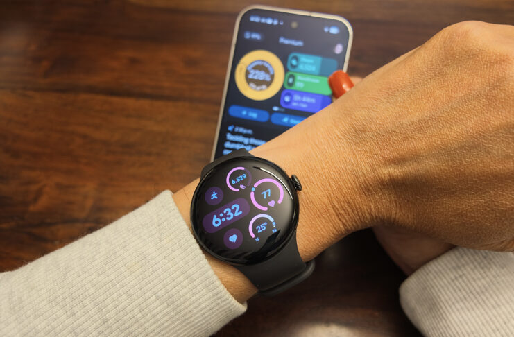 The Google Pixel Watch 5 on an arm with the Google Pixel 11 Pro in the background showing the Google Health app