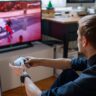 Gamer playing on PS5 with a DualSense wireless controller in front of a TV.
