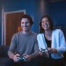 Two people playing PS5 with DualSense wireless controllers.