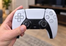 Hand holding a DualSense wireless controller in a living room.