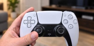 Hand holding a DualSense wireless controller in a living room.