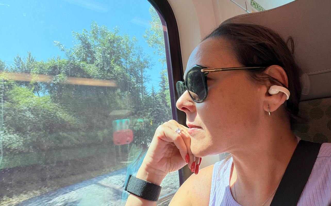 A woman wearing the Sennheiser Momentum Clip earbuds on a train while looking out the window.