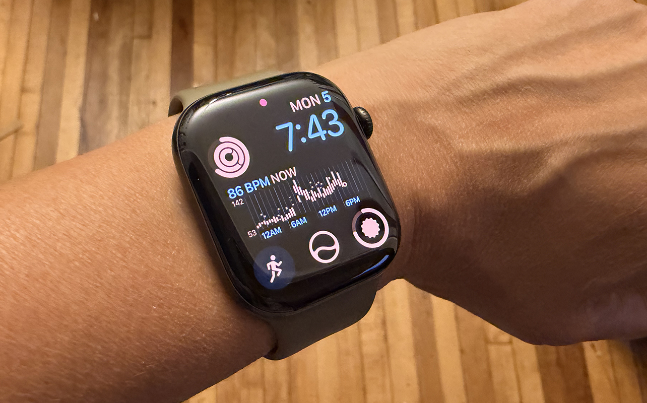 An arm with an Apple Watch Series 12 showing a live heart rate reading.